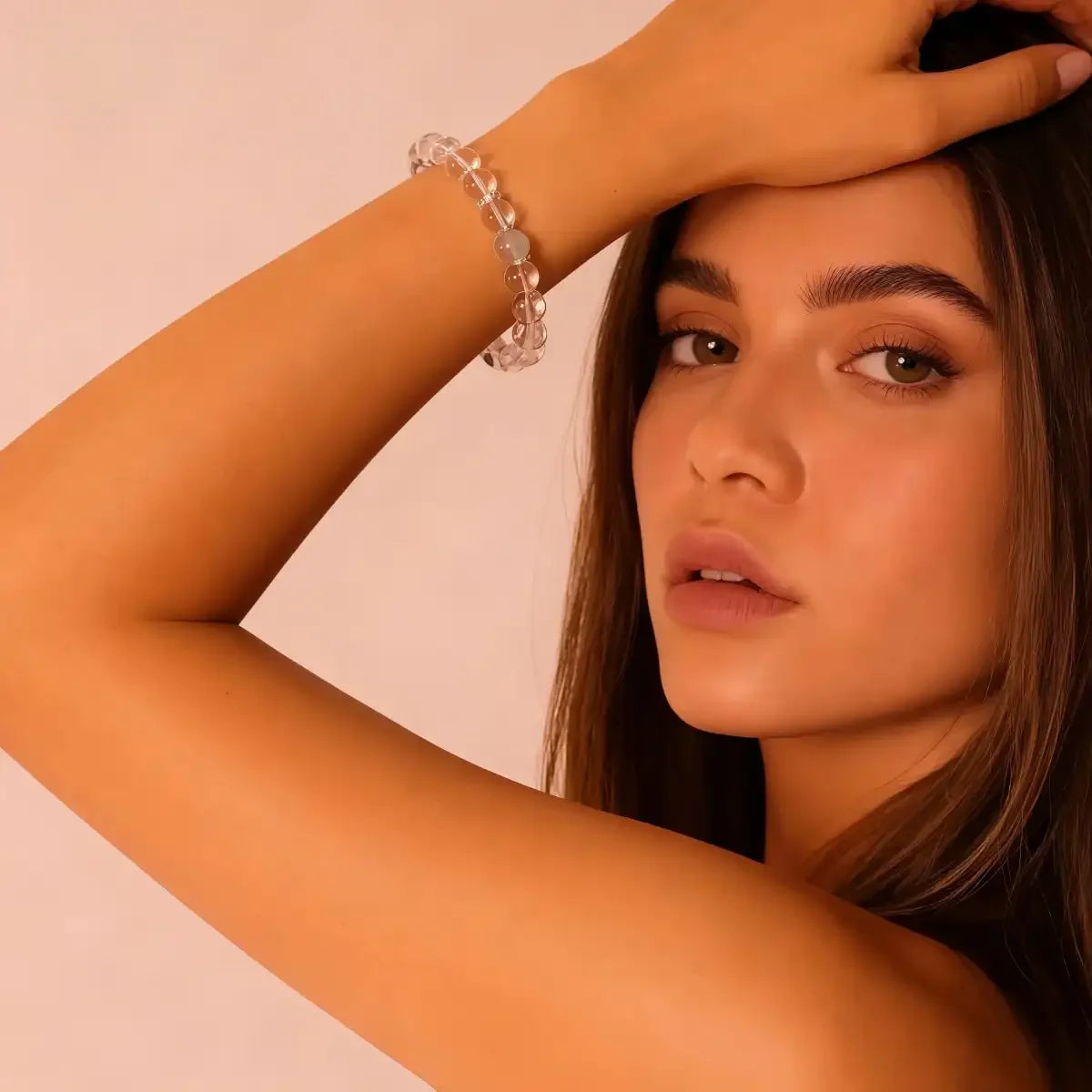 Woman with a clear crystal bracelet on her wrist against a light pink background