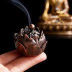 Bronze incense burner shaped like a lotus flower held in a hand with a blurred golden statue in the background.