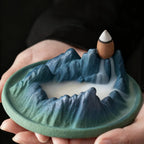 Ceramic mountain landscape with a incense waterfall held in hands against a dark background
