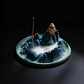 Ceramic incense burner shaped like a mountain with two incense sticks on a dark background
