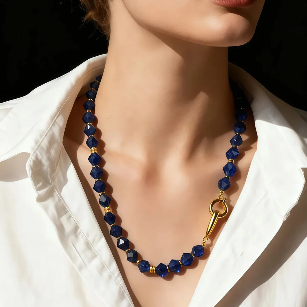 Blue beaded necklace with a gold clasp on a mannequin wearing a white shirt.