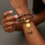 Close-up of a wrist wearing a liuli glass beaded bracelet with a gold charm against a neutral background