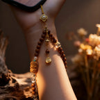 Close-up of a hand holding a wooden beaded Phone Strap with decorative elements against a blurred natural background.