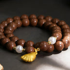 Brown incense beaded bracelet with a gold leaf charm on a dark background