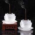 Two white liuli lotus-shaped incense burners with wooden bases on a black background.