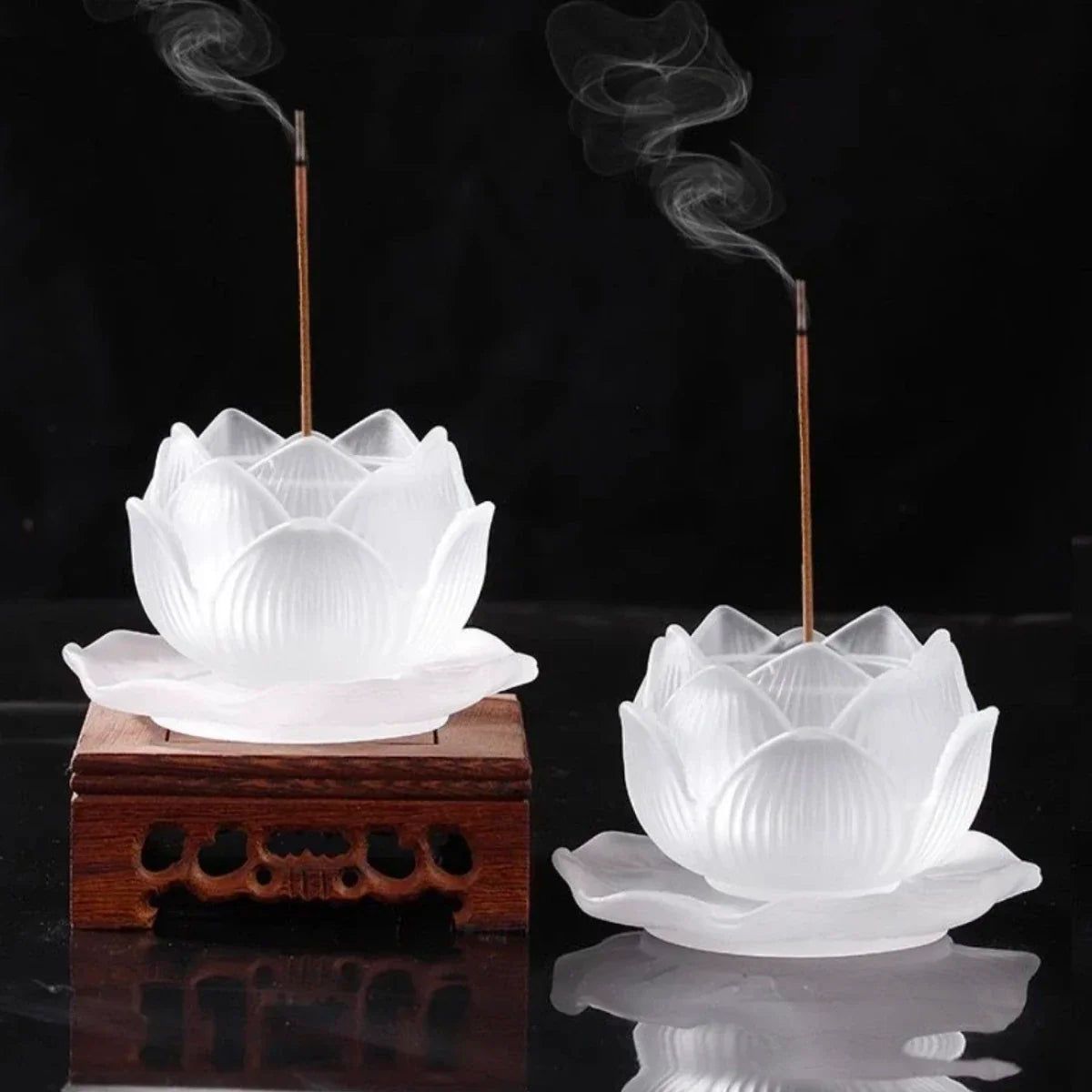 Two white liuli lotus-shaped incense burners with wooden bases on a black background.