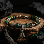 Tibetan Bracelet with green and gold beads and a feather charm on a wooden surface.