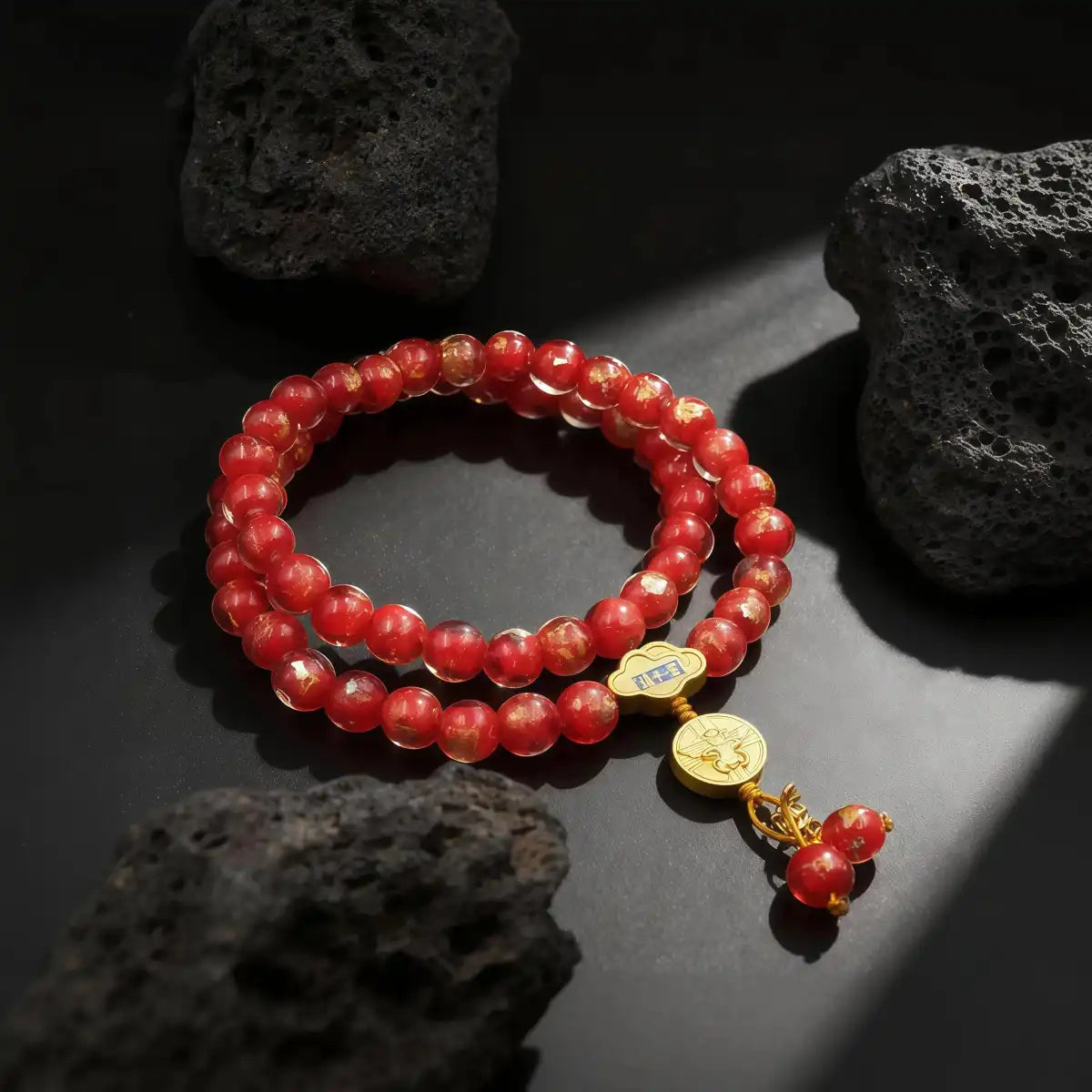 Red liuli glass beaded bracelet with gold charm on a dark surface