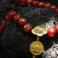 Bracelet with red liuli glass beads and gold medallions on a dark textured surface