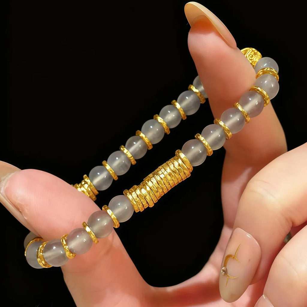 Hand holding a bracelet with gold and gray beads against a black background